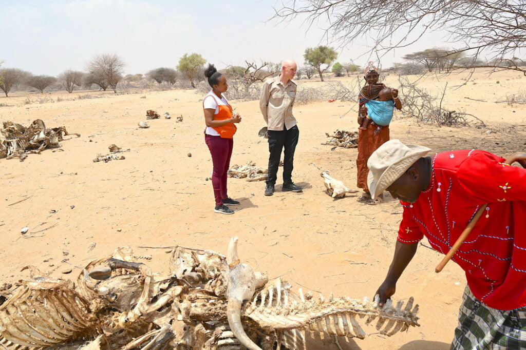 Kansainvälisen World Visionin johtaja Andrew Morley kuuntelee paikallisen kenialaisen tarvinaa keskellä hyvin kuivaa aavikoitunutta maisemaa. Kuvan edustalla näkyy eläimen luuranko.