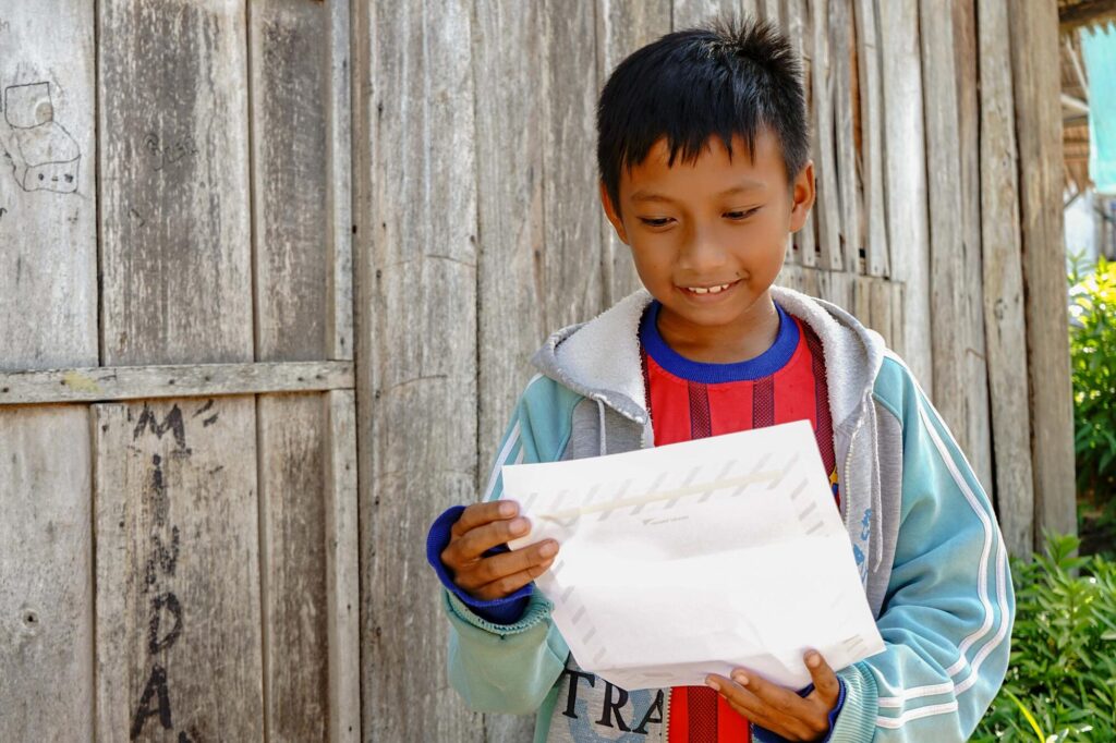 Indonesialainen lapsi pitelee kirjettä kädessään ja hymyilee sitä lukiessaan.