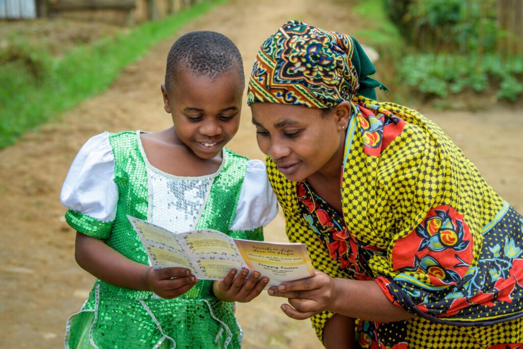 Ruandalainen tyttö ja hänen äitinsä katsovat kirjettä, jonka tyttö on saanut syntymäpäivänään. Lapsella on päällä vihreä paljettimekko ja äidillä värikäs mekko. Takana vehreää maisemaa.