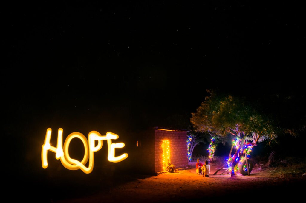 Lapsia puun alla ja valolla piirretty teksti Hope.