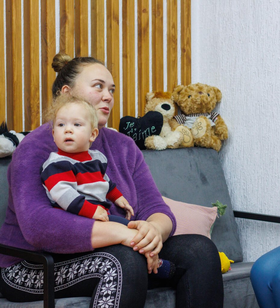 Ukrainalainen äiti pitää taaperoaan sylissä ja juttelee World Visionin vapaaehtoisen kanssa.