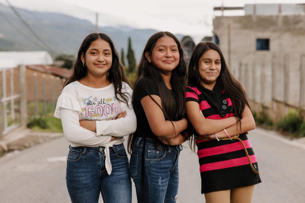 Sheyla, 12 , Guatelmalasta poseeraa itsevarmasti hymyillen kameralle kahden ystävänsä kanssa.