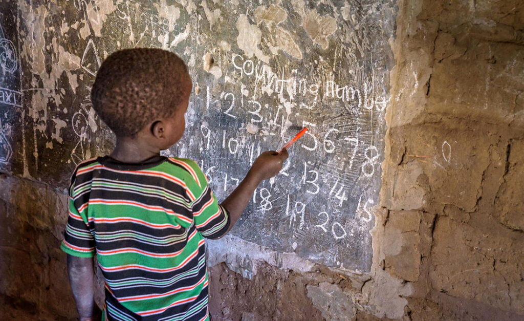 Ugandalainen poika opiskelee luokan taululla numeroita.