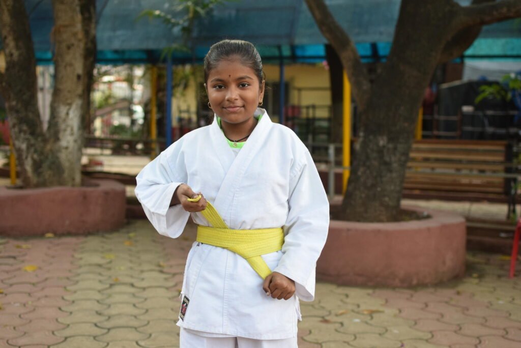 Intialainen tyttö karateasussaan kiristämässä keltaista vyötään.