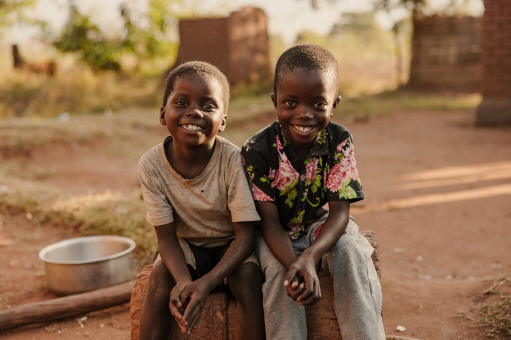 Kaksi lasta istuvat vierekkäin ja hymyilevät kameralle.