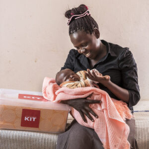 Kenialainen äiti istuu sairaalavuoteella ja hymyilee sylissä olevalle vastasyntyneelle vauvalleen. Hänen vieressä, sängyn päällä, näkyy World Visionilta saatu äitiyspakkaus.