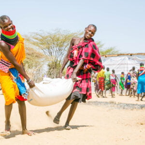 Kaksi kenialaista naista kantavat ruokasäkin välissään.