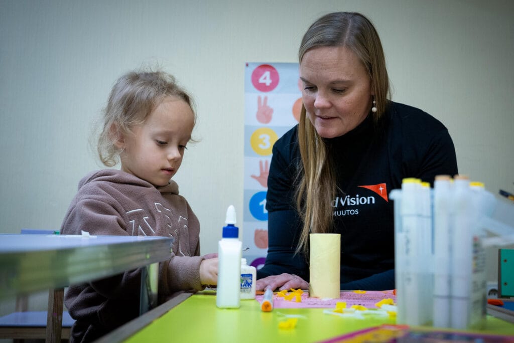 Annette Gothóni askartelemassa ukrainalaisen pikkutytön kanssa lapsiystävällisessä tilassa.